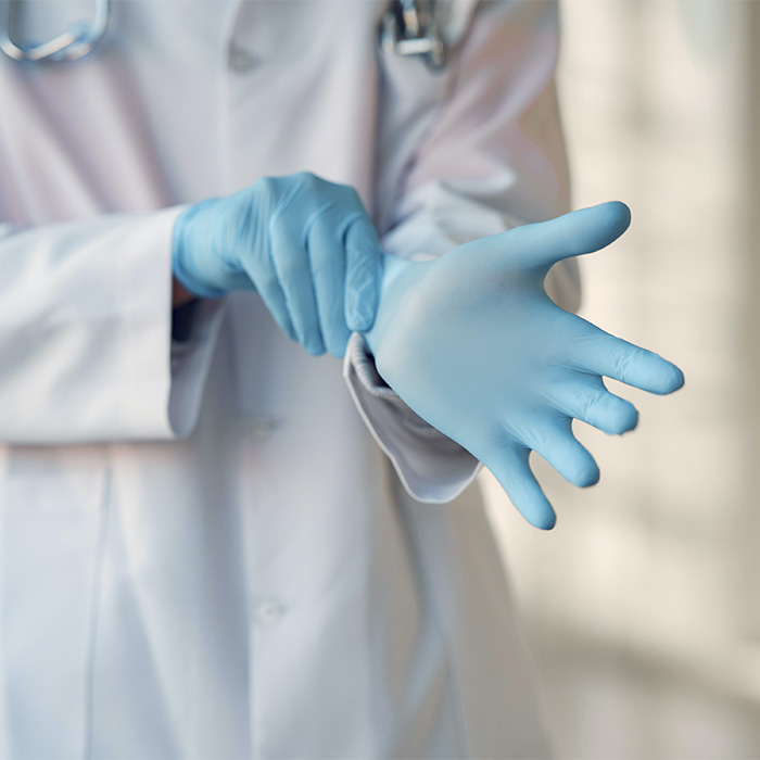 Person in lab coat putting on blue latex gloves